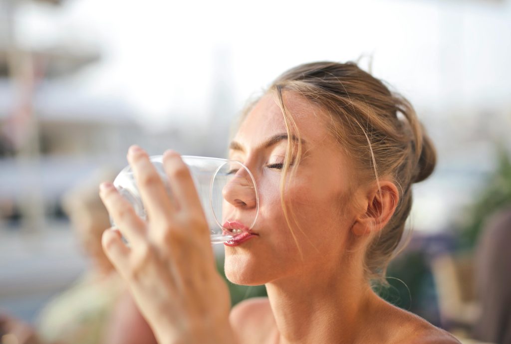 Woman drinking a glass of water outdoors, illustrating the importance of staying hydrated. Drink plenty to keep your liver healthy and support overall wellness.