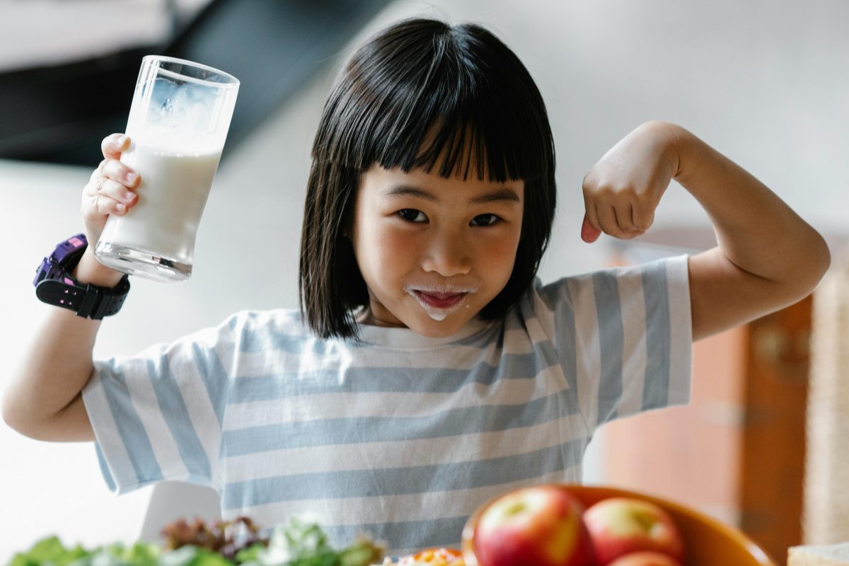Smiling child showing strength while drinking milk, highlighting nutrition for healthy bones.