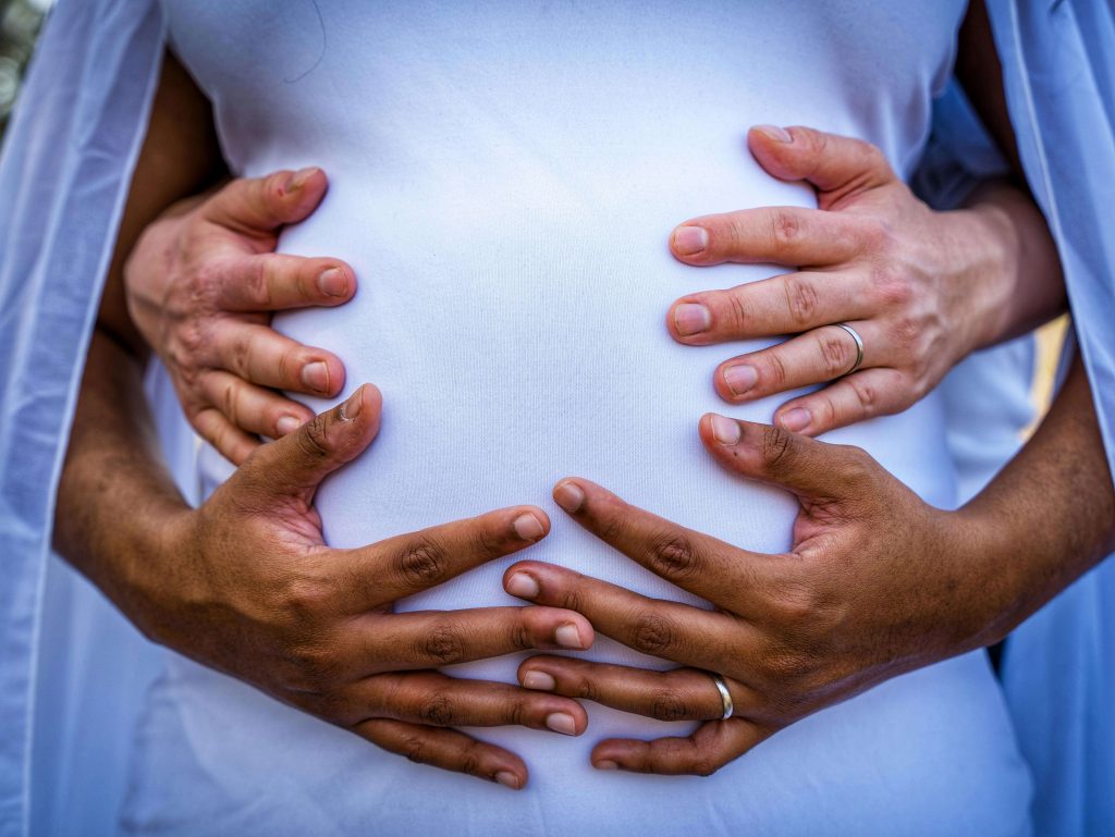 Pair of hands tenderly holding a pregnant belly from both sides.