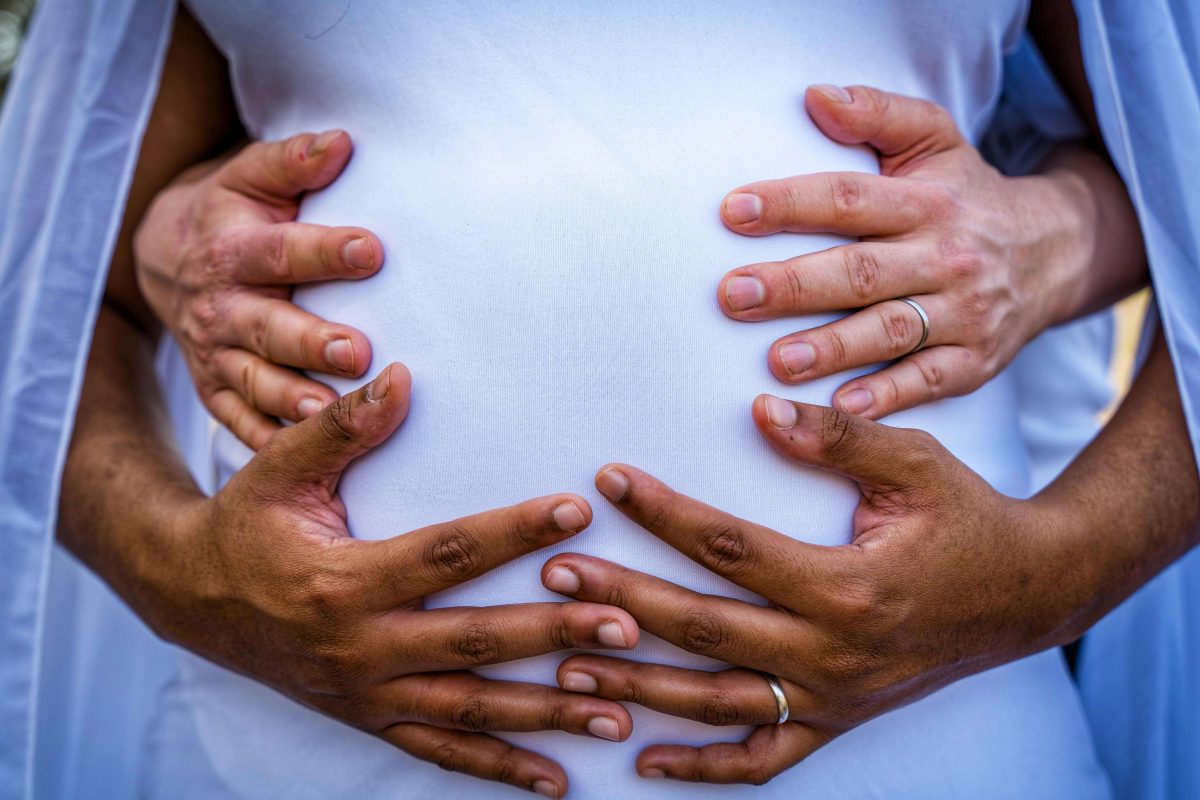 Pair of hands tenderly holding a pregnant belly from both sides.