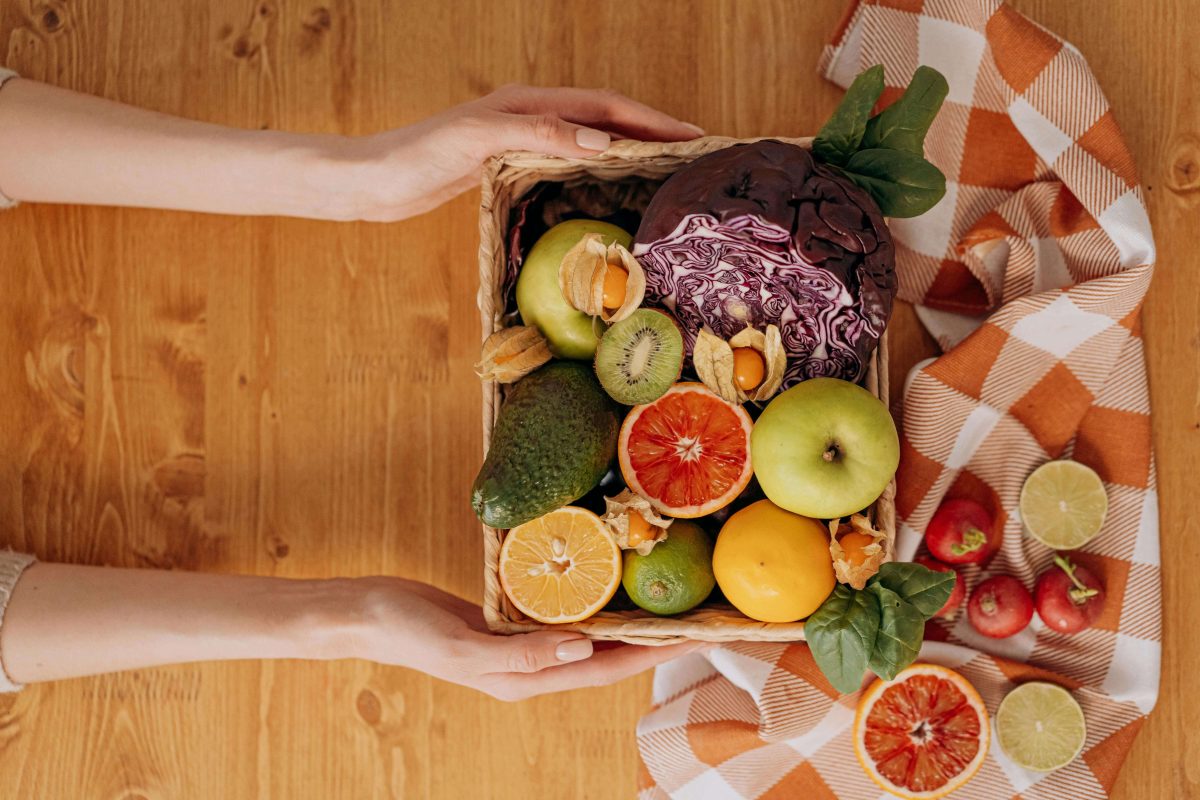 Hands holding a basket of fresh fruits and vegetables to support a healthy and happier lifestyle.